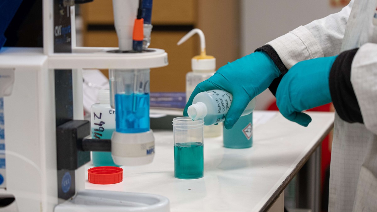 Man pours green liquid into plastic container from the side in laboratory