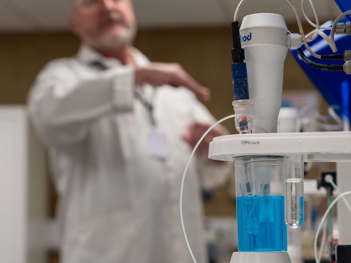 A man talks in the background behind a container with blue liquid